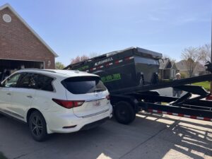A vehicle parked near a dumpster on a trailer being delivered by Utah Valley Dumpsters in Provo, UT.