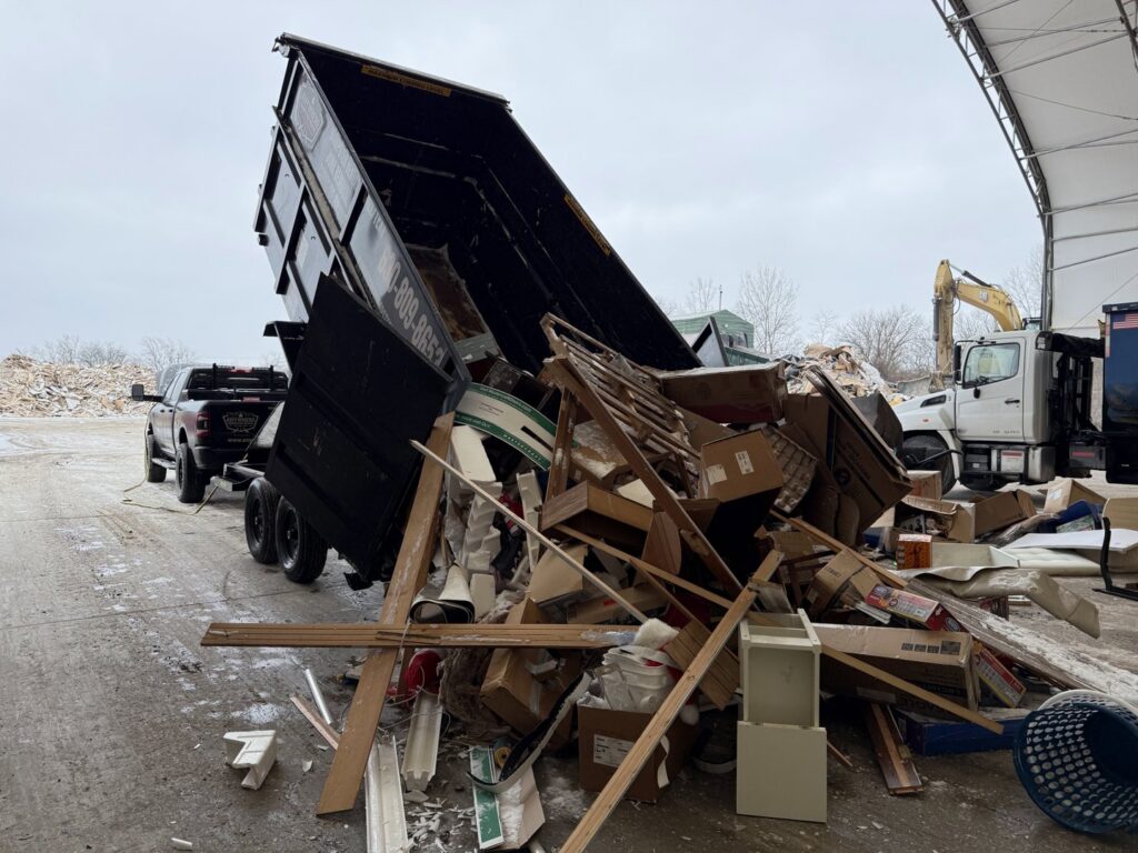 A dumpster trailer dumping construction debris and various junk at a disposal site, showcasing junk removal by Anywhere Dumpster Rental in Naperville, IL.