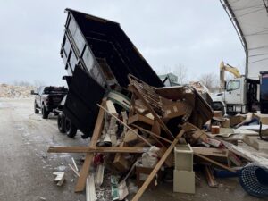 A dumpster trailer dumping construction debris and various junk at a disposal site, showcasing junk removal by Anywhere Dumpster Rental in Naperville, IL.