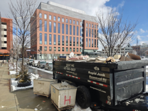 A dumpster trailer from Dumpsters RI.com - Dumpster Rentals RI filled with construction debris on a city street in Rhode Island.