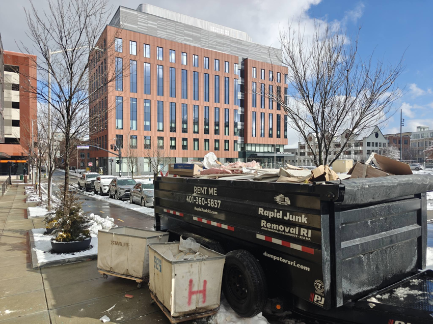A dumpster trailer from Dumpsters RI.com - Dumpster Rentals RI filled with construction debris on a city street in Rhode Island.