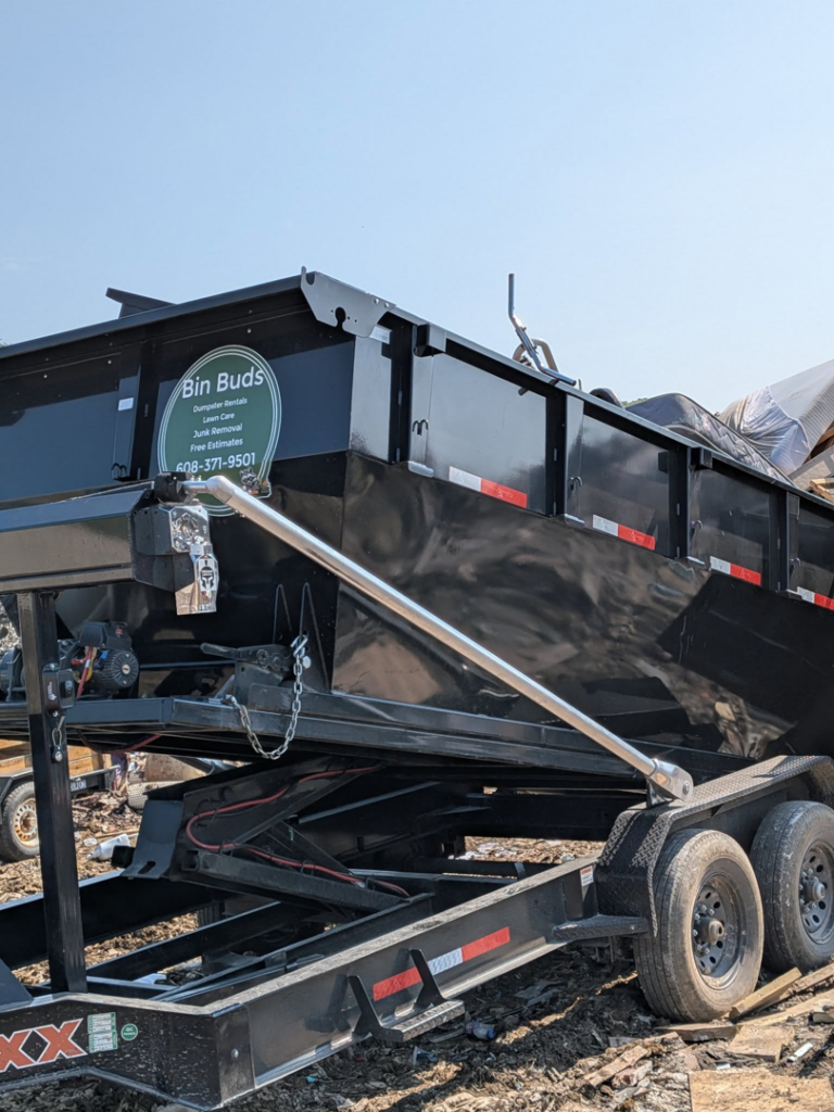 A black dump trailer from Bin Buds Dumpsters, LLC, partially filled with junk, ready for removal in Janesville, WI.