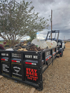 A Highland Dumpster Rentals LLC trailer filled with various junk and debris for removal in Las Cruces, NM.