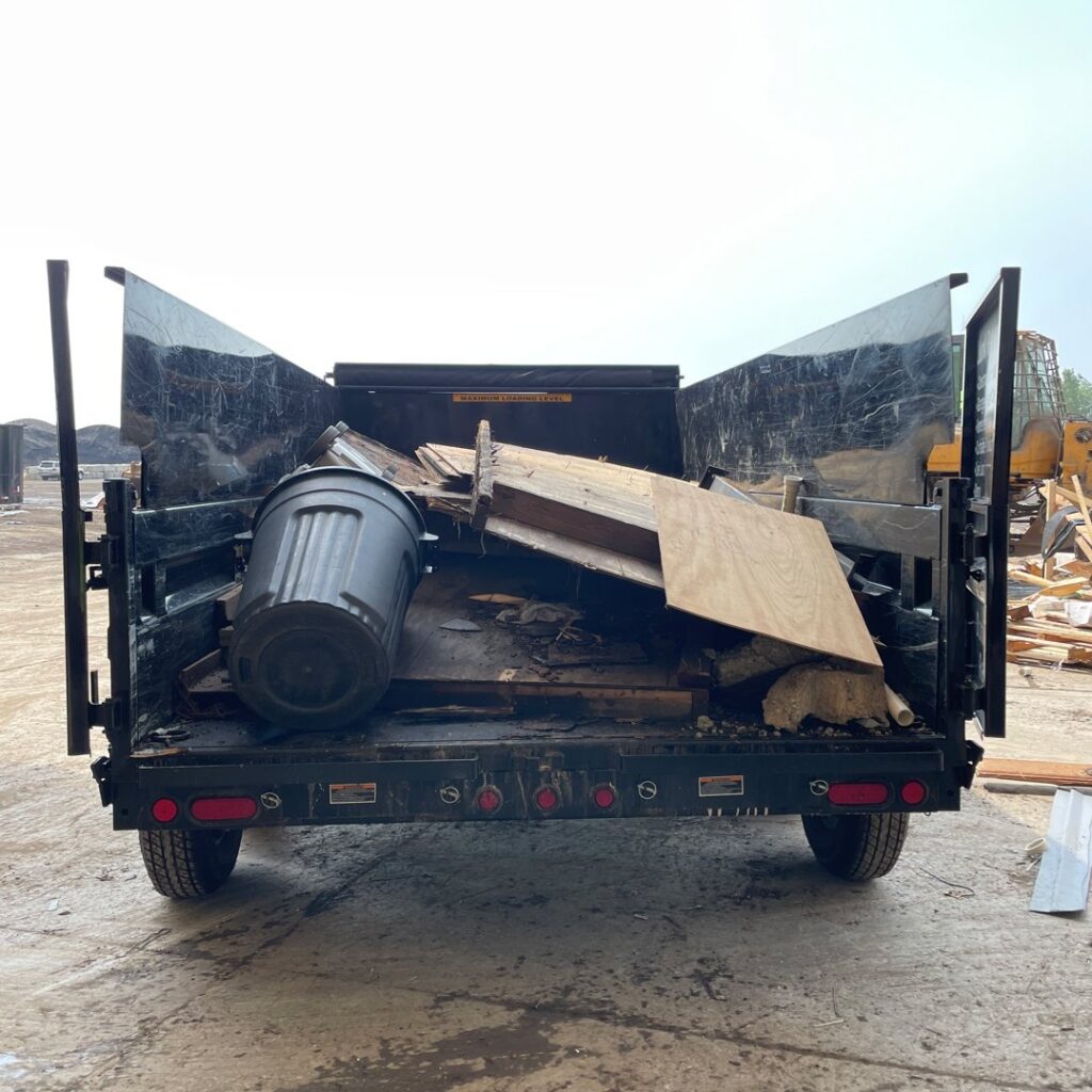 A dumpster trailer filled with various junk, including wood and a trash can, ready for removal by Anywhere Dumpster Rental in Naperville, IL.