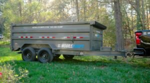 A Mobiledumps dumpster trailer parked in a grassy area, ready for a junk removal job by Mobiledumps Northwest Arkansas in Rogers, AR.