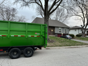 A green dumpster trailer parked on a residential street, ready for a junk removal job by Proper Dumpster Rentals in Kansas City, KS.
