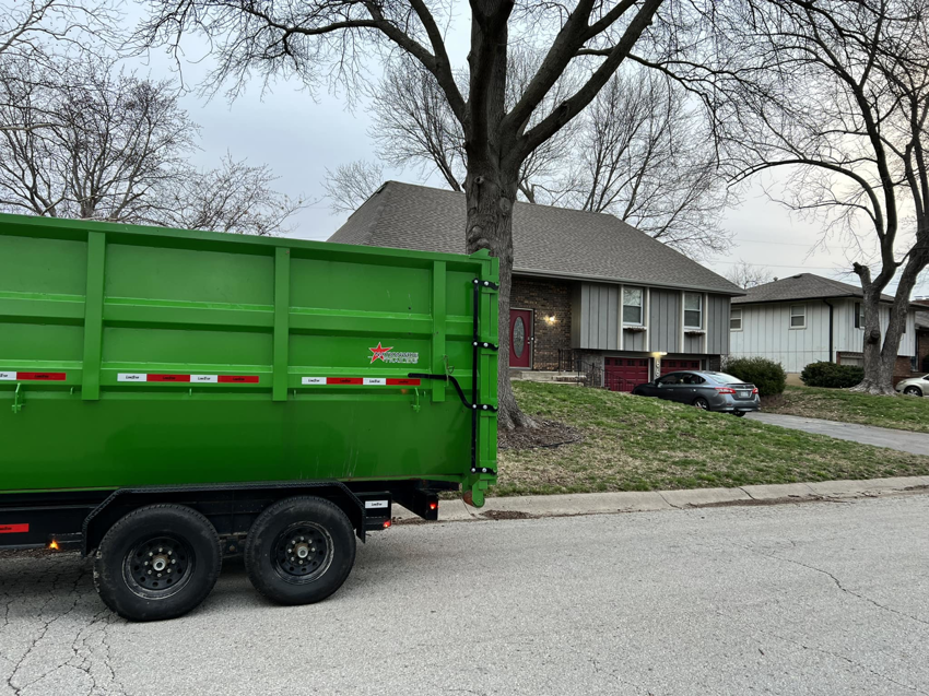 A green dumpster trailer parked on a residential street, ready for a junk removal job by Proper Dumpster Rentals in Kansas City, KS.