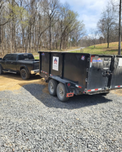 A black dump trailer with the Patriot Dumpster Rental logo being towed by a pickup truck in Chattanooga, TN.
