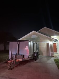 A gray dumpster trailer from Big Skye Dumpsters parked in a residential driveway at night in Jacksonville, FL.