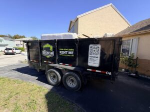 A Driveway Safe Dumpster Rental trailer filled with a mattress and other household junk in a residential driveway in Fort Lauderdale, FL.