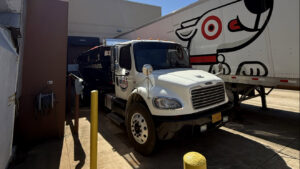 An American Dumpster Rentals truck with a black dumpster backed up to a commercial loading dock in Morrilton, AR.