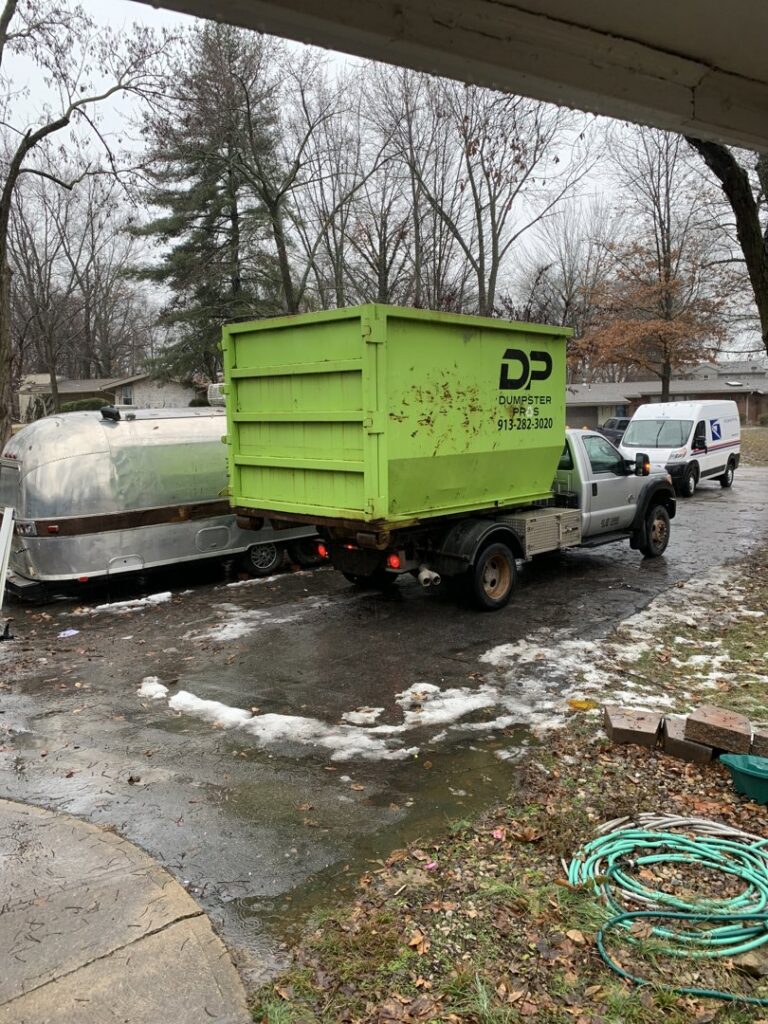 A green dumpster truck from Junk It OR Dump It parked at a residential property in Independence, MO, for junk removal.