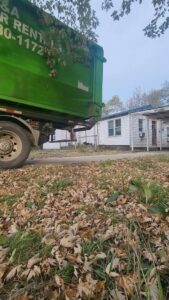 The rear of a J & A Haul Away & Dumpster Rentals truck with a green dumpster near a residential area in Derby, KS.
