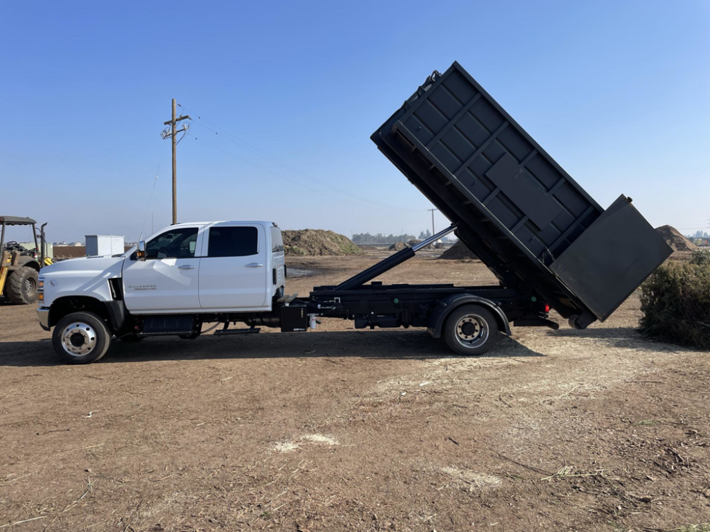 A Valley Dumpster truck actively dumping a load of debris from its black dumpster body in Fresno, CA, demonstrating a general junk removal job.