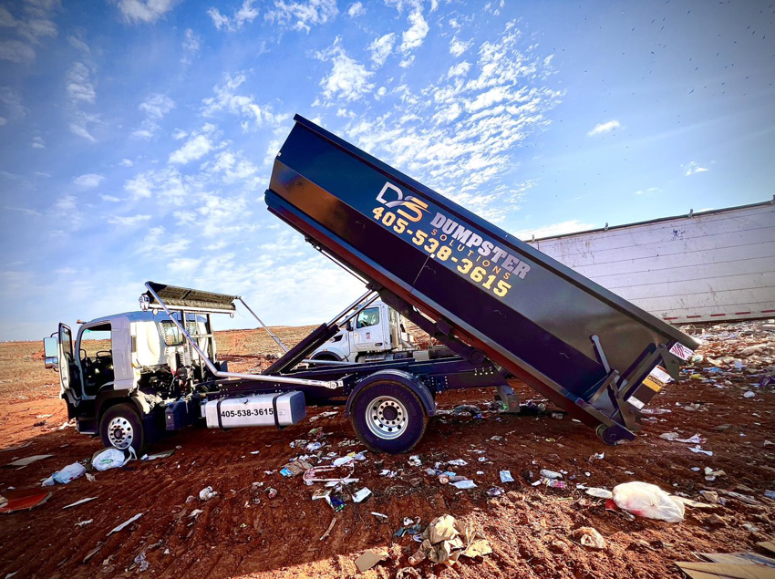 A Dumpster Solutions LLC truck emptying a large dumpster full of waste at a disposal site in Oklahoma City, OK.