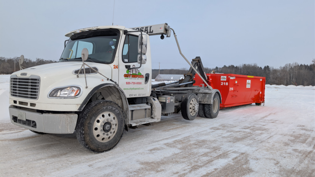A City Disposal Services Inc. dumpster truck with its roll-off mechanism extended, preparing to load or unload a red dumpster in Appleton, WI.