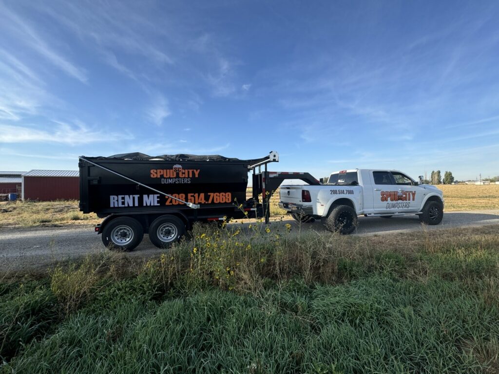 A SpudCity Dumpsters truck pulling a dumpster trailer on a dirt road for a job in Caldwell, ID.