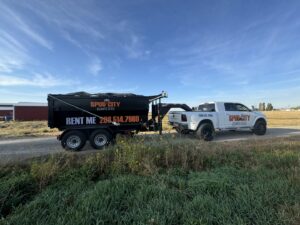 A SpudCity Dumpsters truck pulling a dumpster trailer on a dirt road for a job in Caldwell, ID.