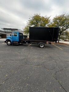 A blue roll-off truck with a black dumpster on its bed, parked in a commercial parking lot by Wagners Property Services LLC in Canton, OH.