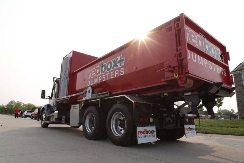 A redbox+ truck transporting a dumpster on a residential street for redbox+ Dumpsters of Greater Austin in Austin, TX