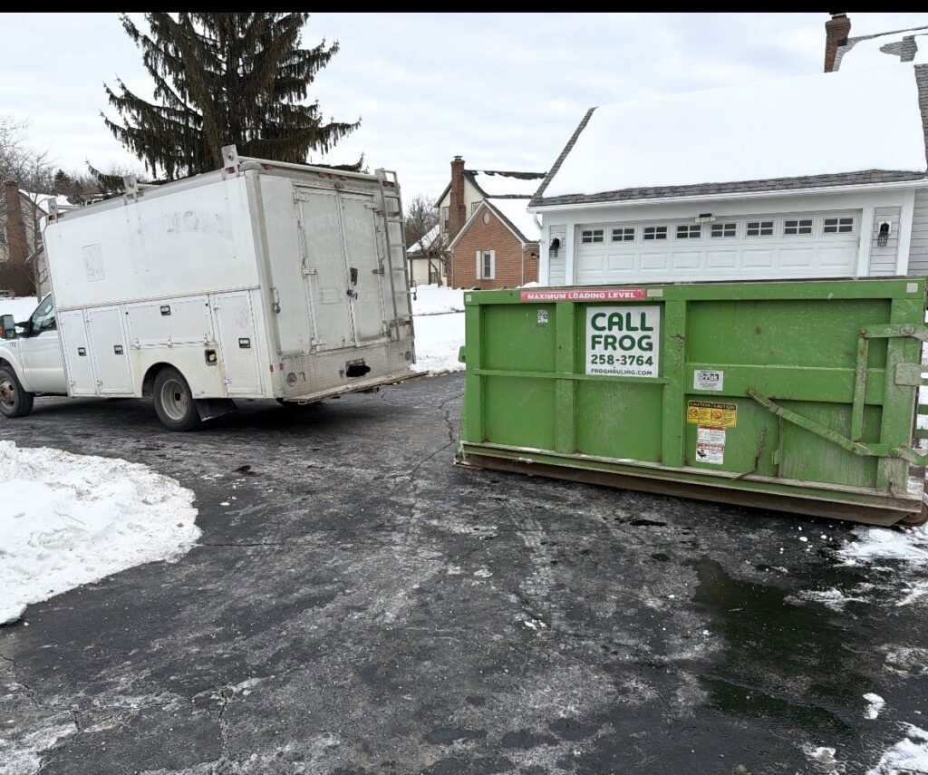 A green Frog Hauling dumpster and service truck in a snowy residential driveway in Columbus, OH.