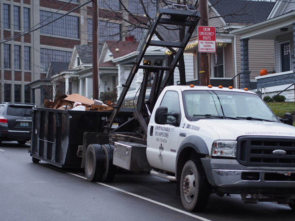 A Dependable Dumpsters truck with a full dumpster of debris on a residential street in Louisville, KY.