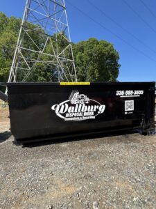 A Wallburg Disposal Worx LLC black dumpster placed under power lines in High Point, NC.