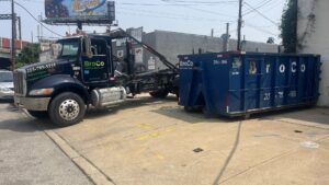 A Broco Waste & Recycling truck unloading a blue dumpster at a commercial site in Warminster, PA.