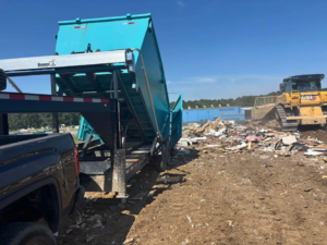 A blue dumpster being unloaded at a demolition site with debris by Site Boss Dumpster Rentals in Raeford, NC.