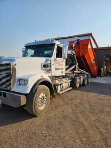 A Rushmore Dumpster truck unloading an orange roll-off dumpster at a waste facility in Rapid City, SD.