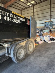 A Bluff City Dumpsters roll-off dumpster next to a large pile of junk inside a warehouse in Memphis, TN.