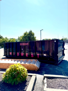 A large black Midwest Containers dumpster with wooden debris next to it, ready for junk removal in Cincinnati, OH.