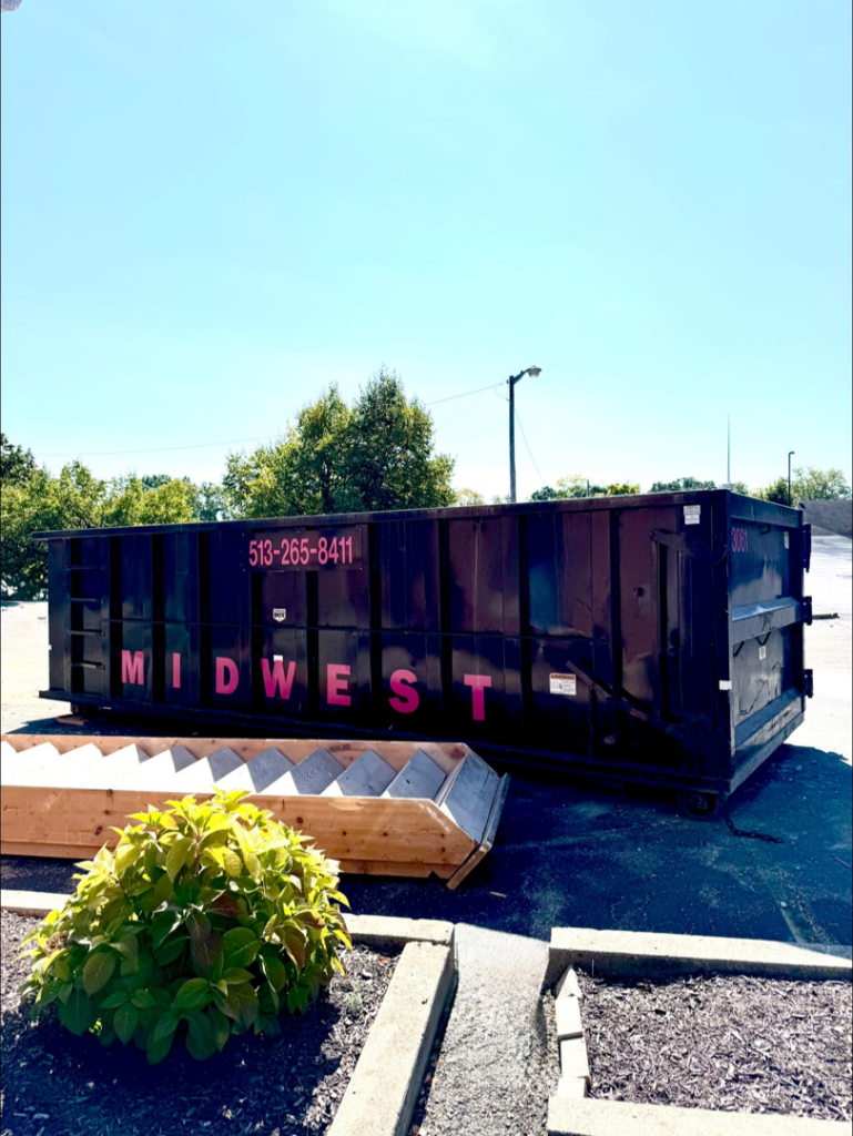 A large black Midwest Containers dumpster with wooden debris next to it, ready for junk removal in Cincinnati, OH.