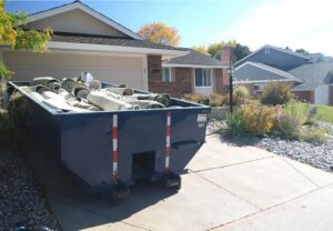A blue roll-off dumpster filled with rolled-up carpets and other debris in a residential driveway for junk removal in Sterling Heights, MI.