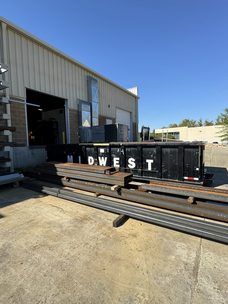 A Midwest Containers dumpster outside a building with scrap metal beams in front, indicating a junk removal job in Cincinnati, OH.