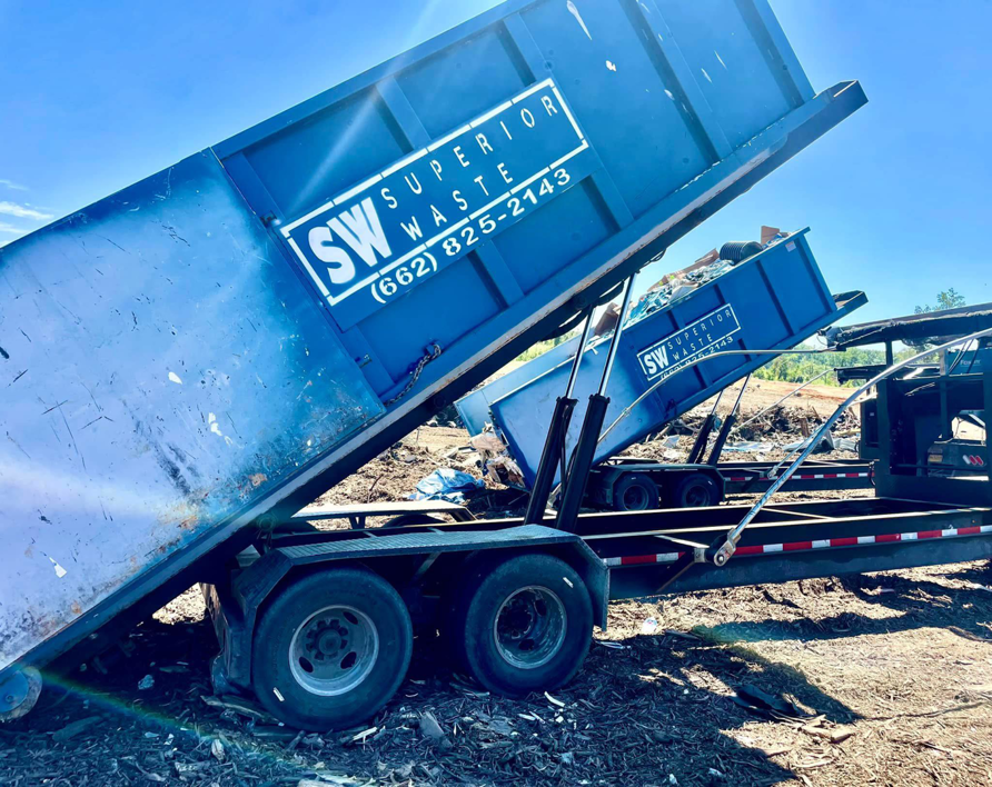 Two blue dumpsters from Superior Waste Management being loaded or unloaded from a trailer for junk removal services in Amory, MS.