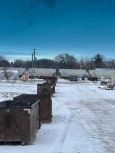 Several dumpsters from NID Dumpster Rental lined up in a snowy industrial area with train cars in Nashua, IA.