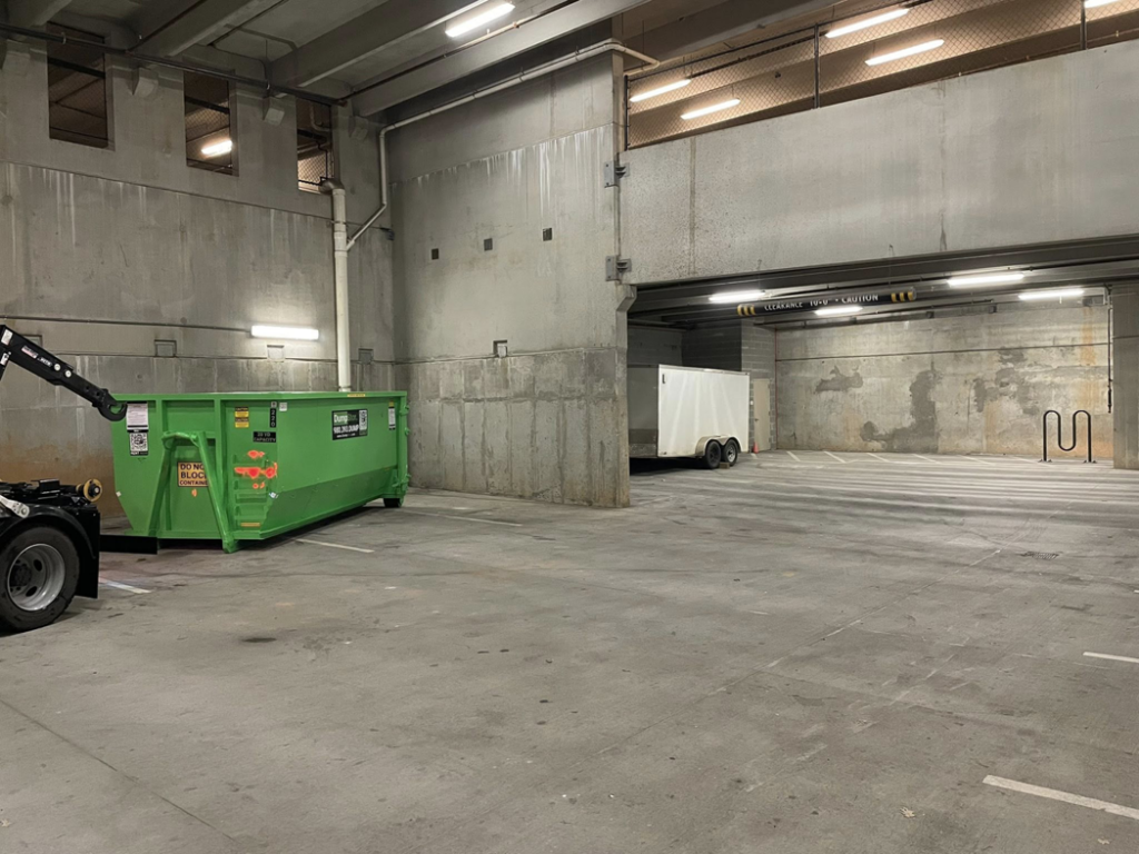 A DumpStor green dumpster being delivered or picked up by a truck in an underground parking garage in Charlotte, NC.