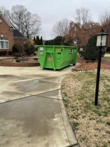A green DumpStor dumpster placed on a large residential driveway, ideal for home cleanouts in Charlotte, NC.