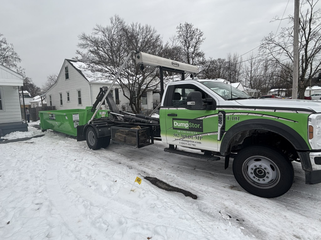 A DumpStor of Louisville truck delivering a green dumpster to a residential property on a snowy day in Louisville, KY.