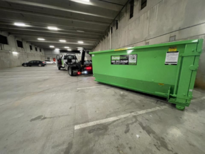 A DumpStor truck with a green dumpster in an underground parking garage, ready for service in Charlotte, NC.