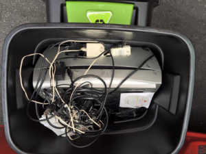 A black recycling bin filled with old electronics and tangled cables, ready for e-waste removal by E-Grove in Minneapolis, MN.