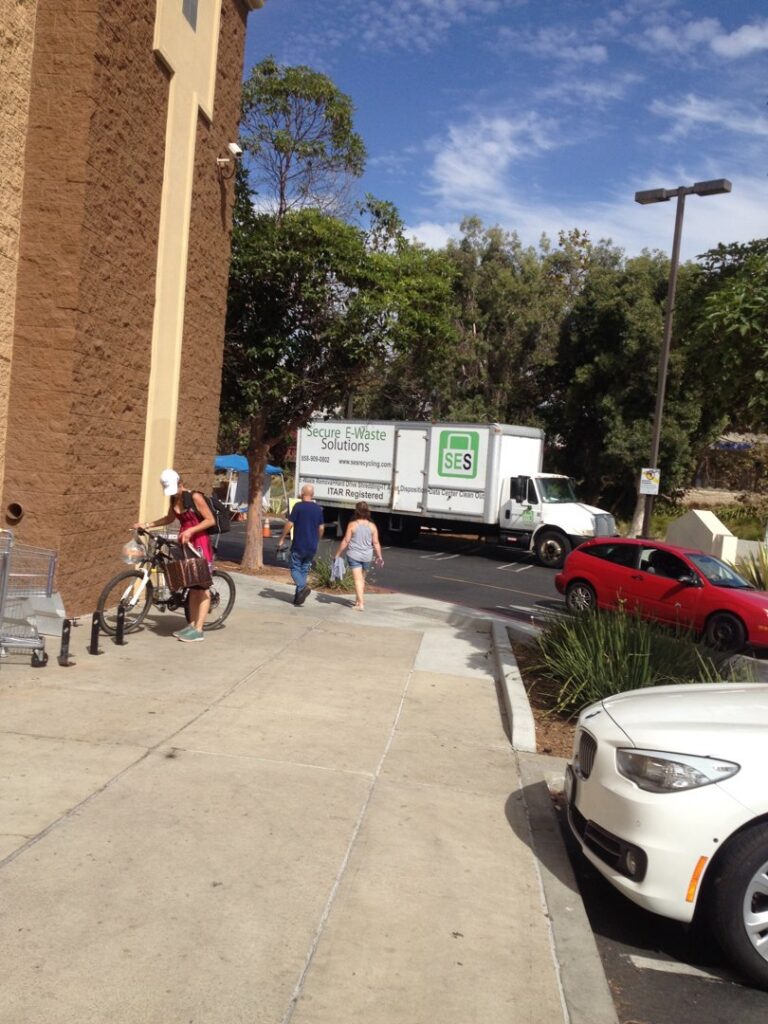 A sign detailing pricing for e-waste collection at an outdoor event by SES Secure E-Waste Solutions Inc. in San Diego, CA.