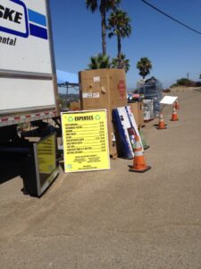 A sign detailing expenses for e-waste recycling at an outdoor collection event by SES Secure E-Waste Solutions Inc. in San Diego, CA.