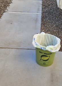 A green EcoSmart bucket with a trash bag liner, ready for pet waste removal services by EcoScoops Pet Waste Removal in Gilbert, AZ.
