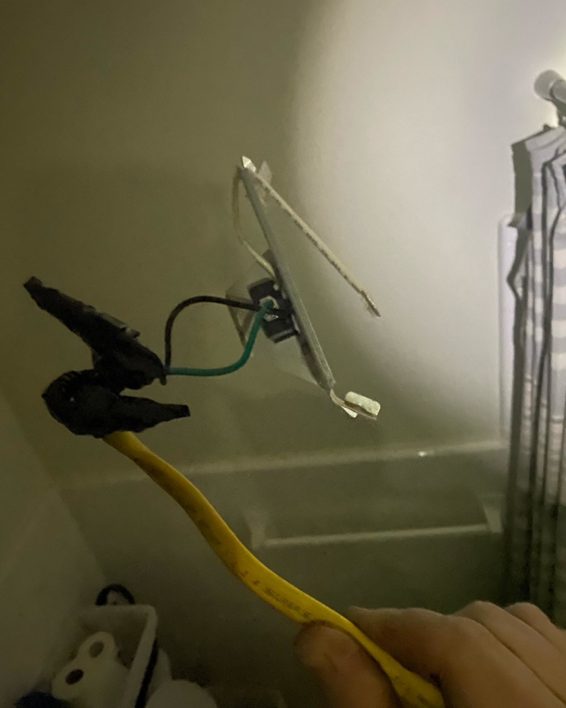 A hand holding an electrical outlet with exposed wiring during a repair by Gingy's Electrical Services, LLC in Memphis, TN.