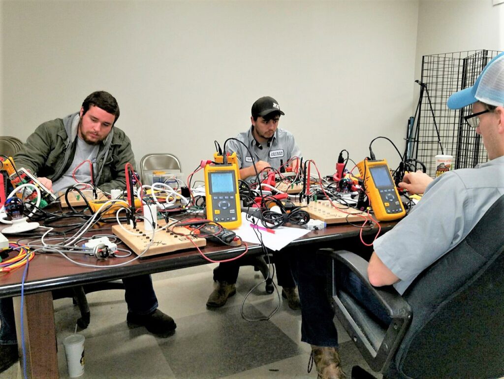 Electrical technicians working with testing equipment and wiring on a table at Joyner Electric And Security in Savannah, GA.