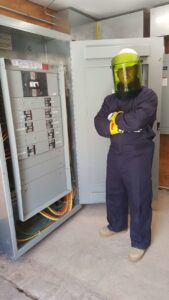 An electrician in arc flash PPE next to an open electrical panel, demonstrating safety by Denali Electric LLC in San Antonio, TX