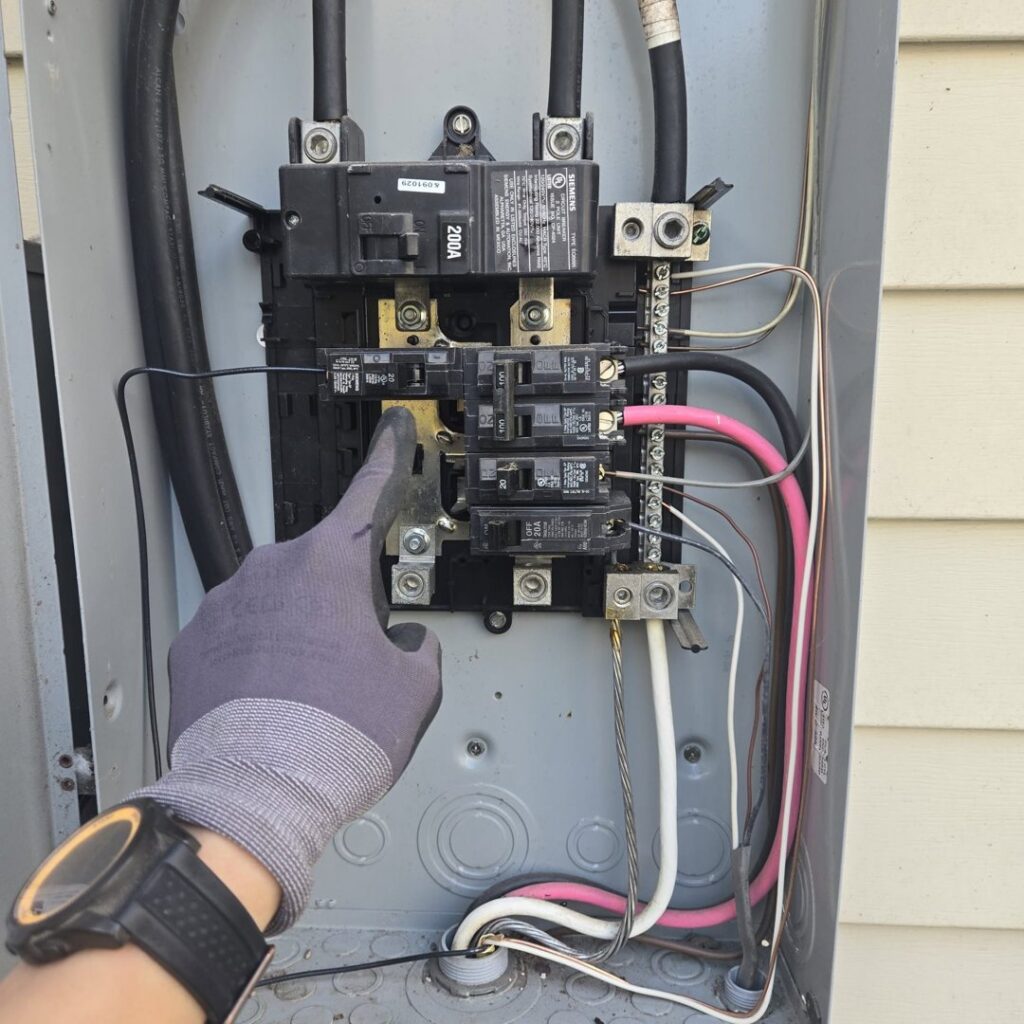 An electrician's gloved hand pointing to a circuit breaker in an open electrical panel by Joyner Electric And Security in Savannah, GA.