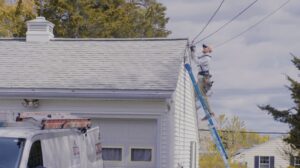 An electrician on a ladder performing exterior wiring work on a house for Paul Bergeron Jr. Contracting Inc. in Worcester, MA